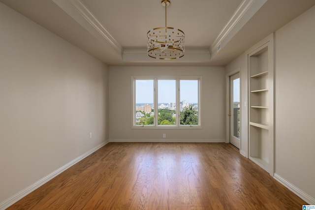 spare room featuring built in features, a chandelier, hardwood / wood-style flooring, ornamental molding, and a raised ceiling