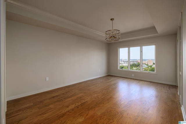 unfurnished room featuring crown molding, hardwood / wood-style floors, a tray ceiling, and a notable chandelier