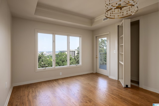 empty room with ornamental molding, light wood-type flooring, and a tray ceiling