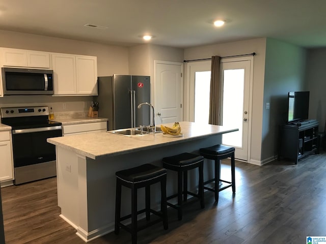 kitchen featuring dark wood-type flooring, stainless steel appliances, an island with sink, sink, and white cabinetry