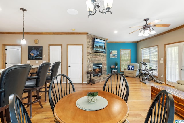 dining area featuring ceiling fan with notable chandelier, a fireplace, light wood-type flooring, and ornamental molding