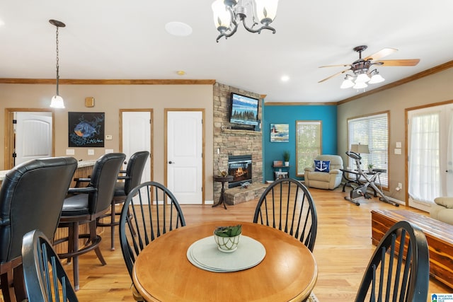 dining space featuring crown molding, a fireplace, ceiling fan with notable chandelier, and light wood-type flooring