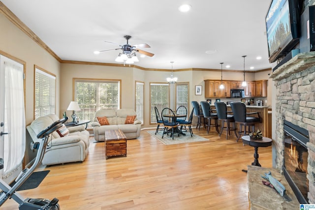 living room with crown molding, a fireplace, ceiling fan with notable chandelier, and light hardwood / wood-style flooring