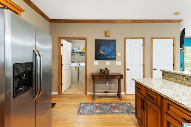 kitchen featuring washing machine and clothes dryer, light stone counters, stainless steel fridge with ice dispenser, crown molding, and light wood-type flooring