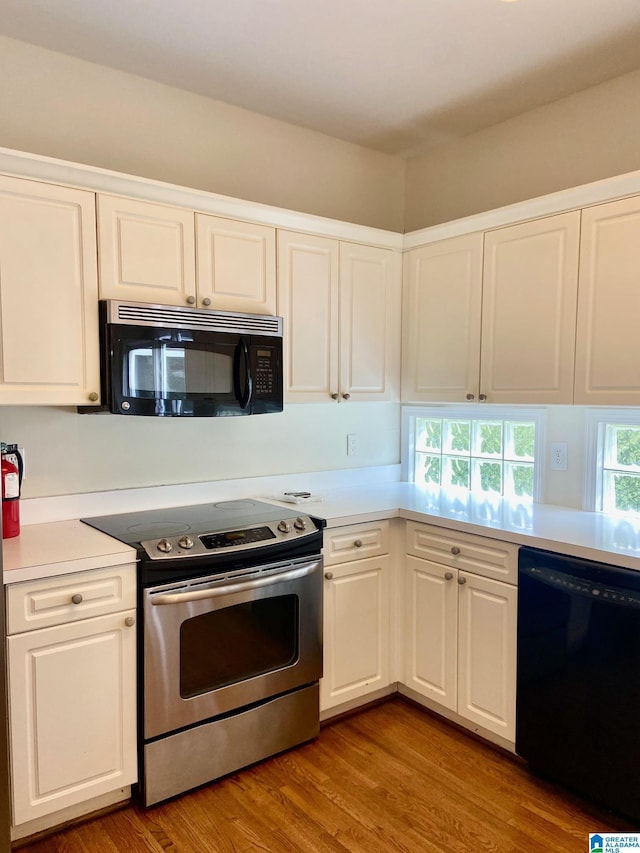 kitchen with white cabinets, light countertops, black appliances, and wood finished floors