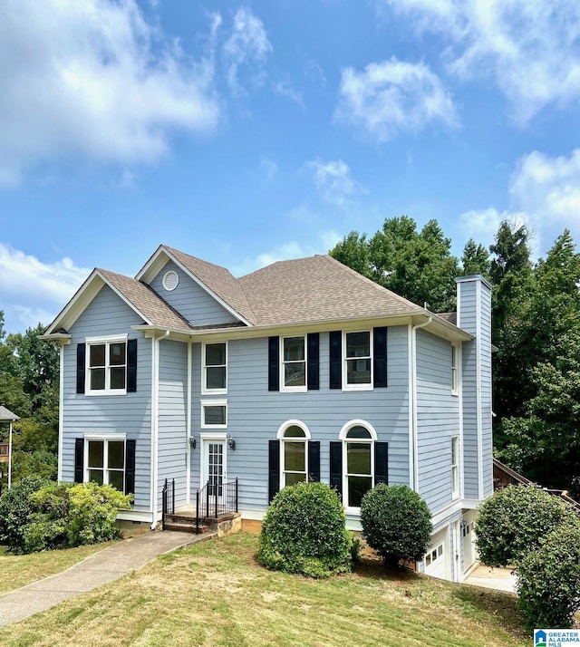 view of front facade featuring a shingled roof, an attached garage, a chimney, and a front lawn