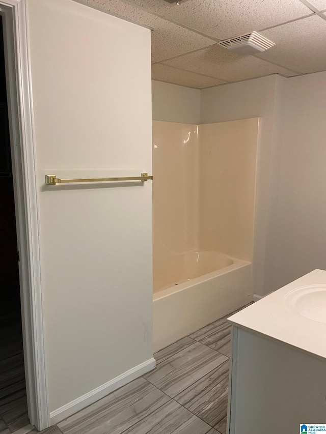 full bathroom with a paneled ceiling, vanity, visible vents, baseboards, and shower / washtub combination