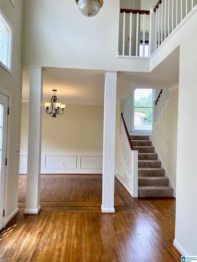 foyer featuring decorative columns, a notable chandelier, hardwood / wood-style floors, and a towering ceiling