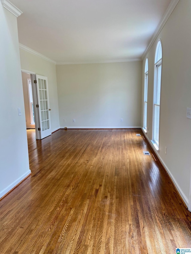 empty room with ornamental molding, visible vents, dark wood finished floors, and baseboards