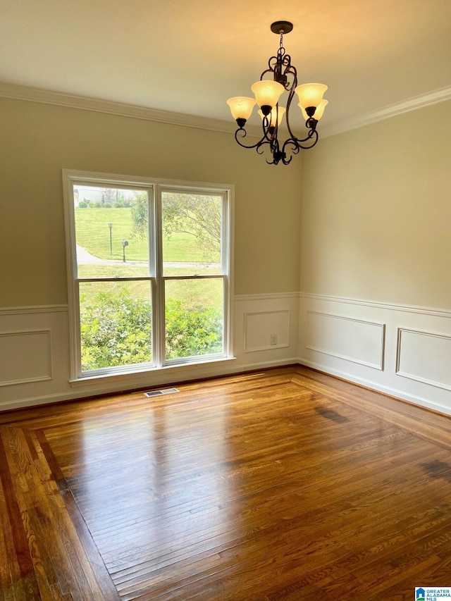 spare room featuring visible vents, wainscoting, wood finished floors, crown molding, and a chandelier