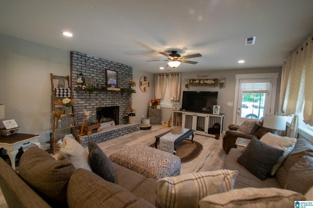 living room featuring a fireplace, light hardwood / wood-style flooring, ceiling fan, and brick wall