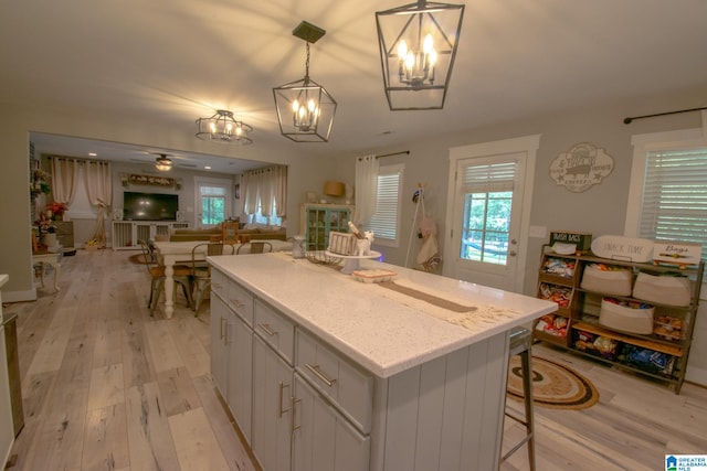 kitchen featuring light hardwood / wood-style flooring, pendant lighting, a kitchen island, ceiling fan with notable chandelier, and a breakfast bar area