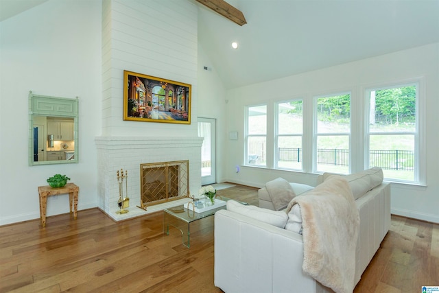 living room with beam ceiling, high vaulted ceiling, a brick fireplace, and light hardwood / wood-style floors