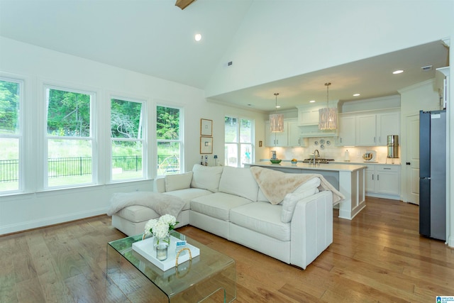 living room with high vaulted ceiling, light wood-type flooring, and sink