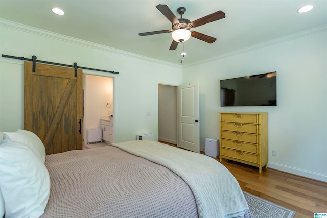 bedroom featuring a barn door, wood-type flooring, ceiling fan, ornamental molding, and ensuite bathroom