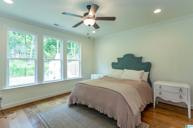 bedroom with ceiling fan, multiple windows, light hardwood / wood-style floors, and ornamental molding