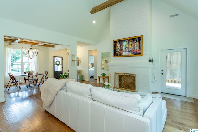 living room featuring a brick fireplace, a notable chandelier, high vaulted ceiling, light hardwood / wood-style flooring, and beamed ceiling