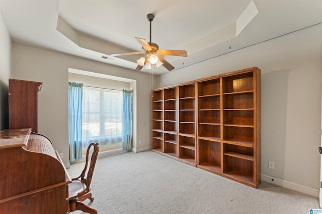 carpeted home office featuring a tray ceiling and ceiling fan