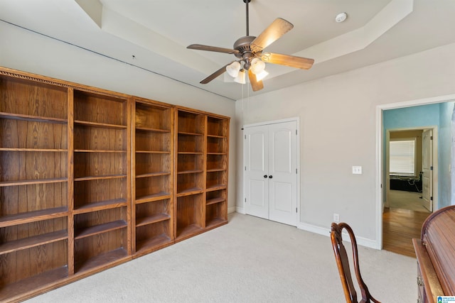 office space with light carpet, ceiling fan, and a raised ceiling