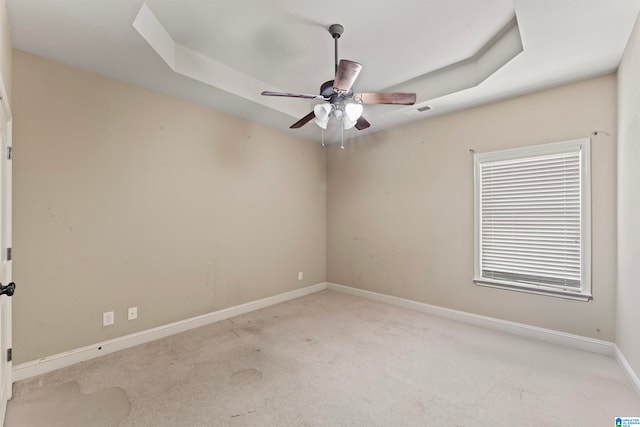 carpeted spare room with ceiling fan and a raised ceiling