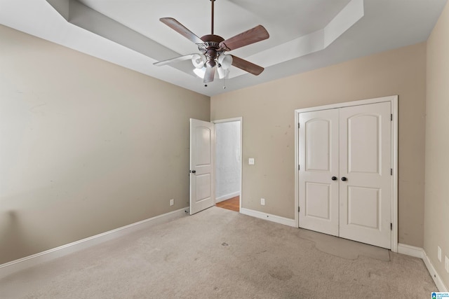 unfurnished bedroom with a tray ceiling, light colored carpet, a closet, and ceiling fan