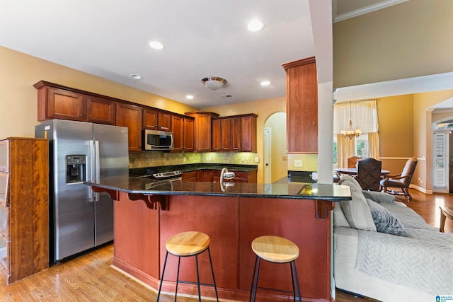 kitchen featuring kitchen peninsula, light hardwood / wood-style floors, stainless steel appliances, decorative backsplash, and a breakfast bar