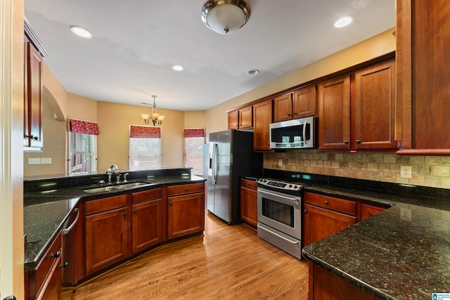 kitchen with appliances with stainless steel finishes, dark stone counters, sink, and light wood-type flooring