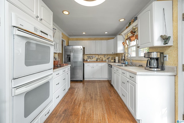 kitchen with appliances with stainless steel finishes, white cabinetry, crown molding, hardwood / wood-style flooring, and sink