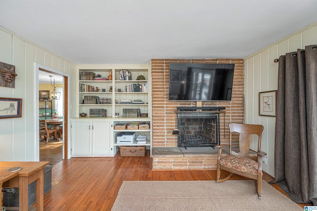 living room featuring light wood-type flooring, wooden walls, and a brick fireplace