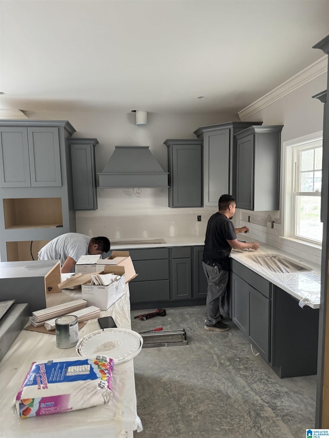 kitchen featuring custom range hood, light countertops, gray cabinets, tasteful backsplash, and crown molding