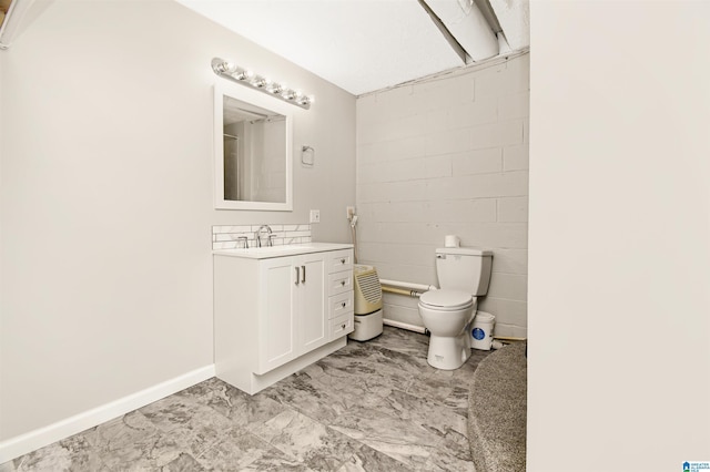 bathroom featuring concrete block wall, baseboards, vanity, and toilet