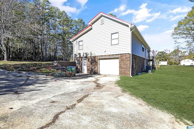 view of side of property featuring brick siding, a yard, an attached garage, cooling unit, and driveway