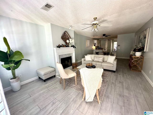 living room with a fireplace, ceiling fan, light wood-type flooring, and a textured ceiling