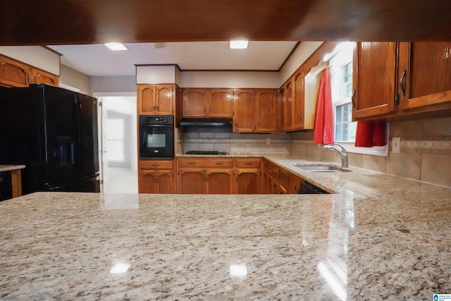 kitchen with decorative backsplash, light stone counters, sink, and black appliances