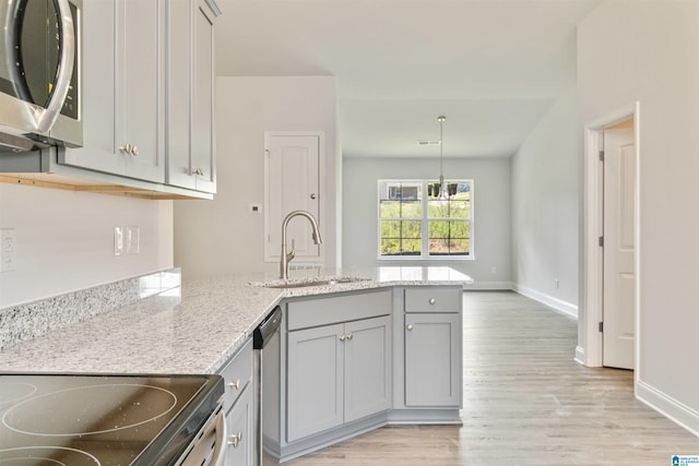 kitchen featuring appliances with stainless steel finishes, kitchen peninsula, light stone countertops, light wood-type flooring, and sink