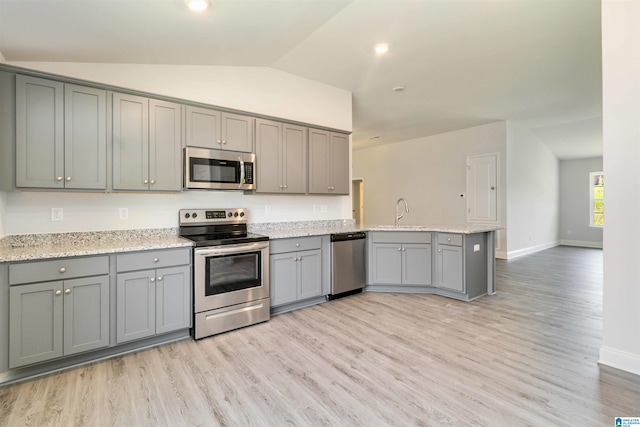 kitchen with lofted ceiling, light wood-type flooring, stainless steel appliances, and light stone countertops