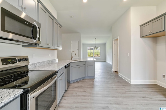 kitchen featuring light wood-type flooring, stainless steel appliances, sink, and light stone counters