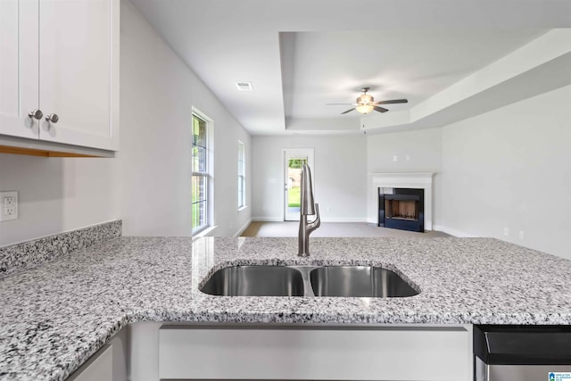 kitchen featuring a tray ceiling, light stone counters, sink, and white cabinets