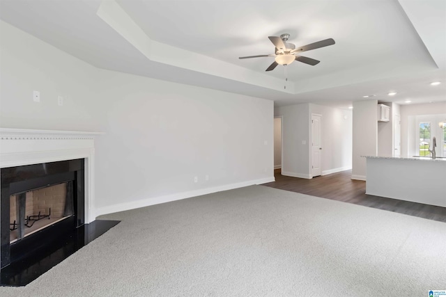 living room featuring ceiling fan, dark carpet, and a raised ceiling