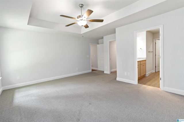 unfurnished bedroom featuring a raised ceiling, ensuite bath, ceiling fan, and light carpet