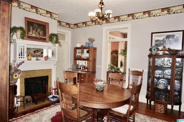 dining area with a textured ceiling, a fireplace, hardwood / wood-style floors, and an inviting chandelier