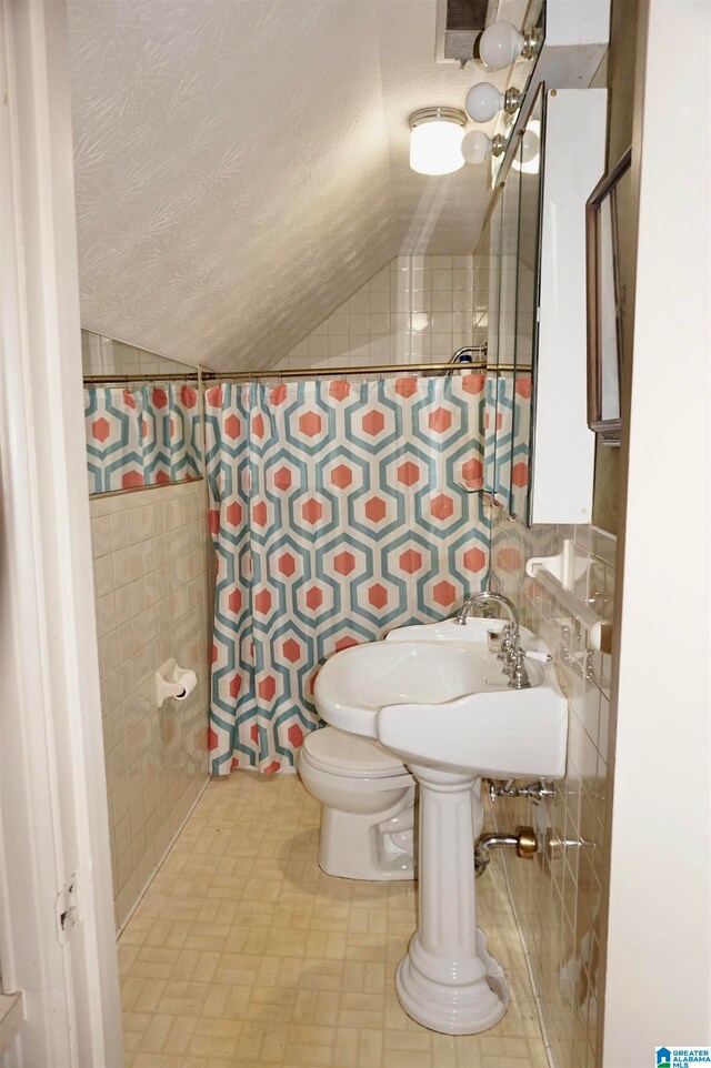 bathroom featuring tile patterned floors, vaulted ceiling, toilet, and tile walls