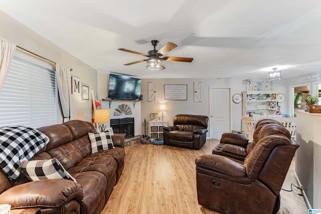 living area featuring a fireplace with raised hearth, ceiling fan, and light wood-type flooring