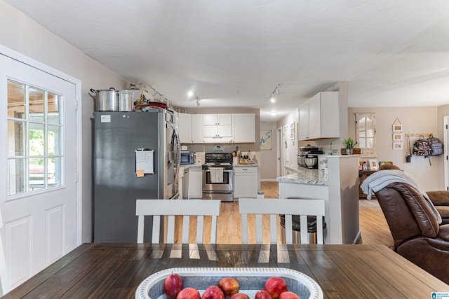 kitchen with light stone counters, stainless steel appliances, white cabinetry, open floor plan, and light wood-type flooring