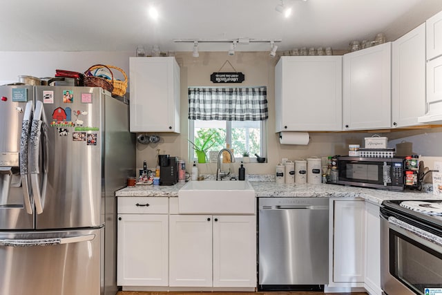 kitchen with stainless steel appliances, white cabinetry, a sink, and light stone counters