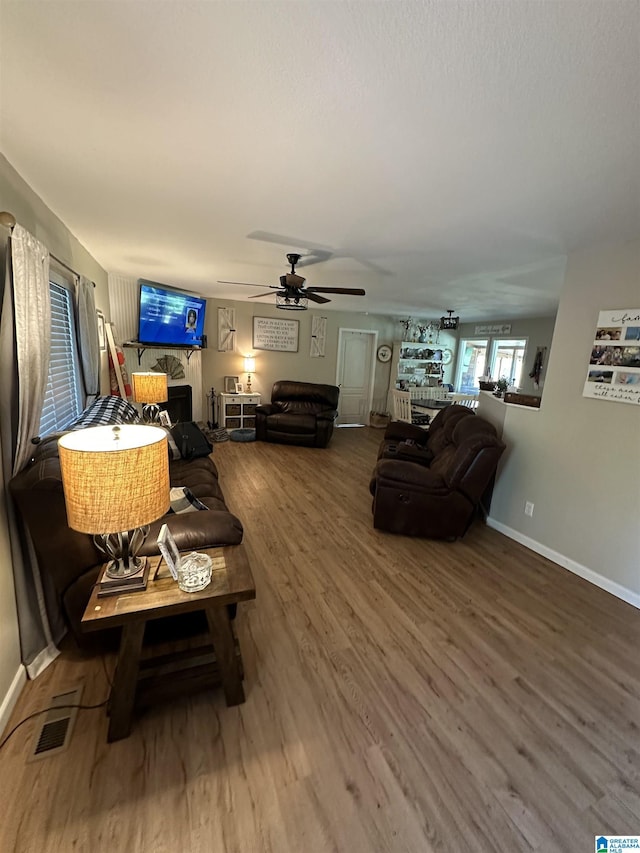 living room featuring ceiling fan, wood finished floors, visible vents, and baseboards