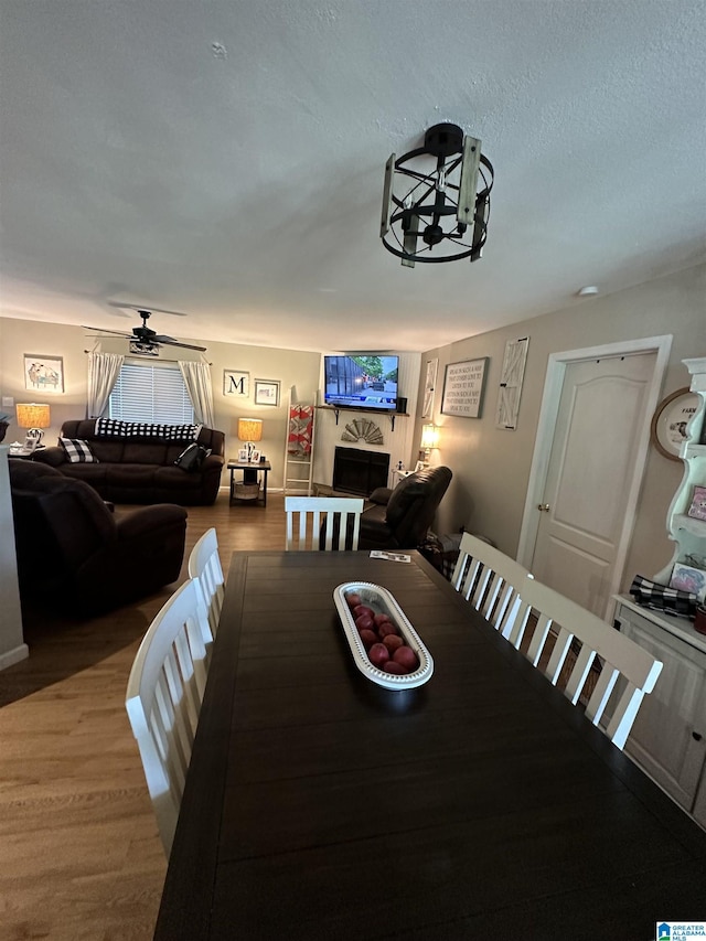 dining room featuring a textured ceiling, a fireplace, wood finished floors, and a ceiling fan