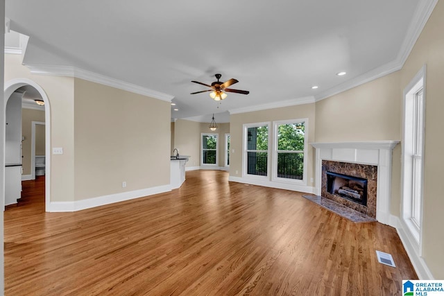 unfurnished living room featuring ceiling fan, crown molding, a fireplace, and light hardwood / wood-style flooring