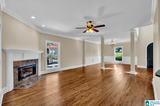 unfurnished living room with wood-type flooring, a fireplace, ceiling fan with notable chandelier, and a healthy amount of sunlight