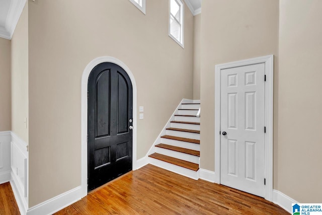 foyer featuring wood-type flooring, ornamental molding, and a high ceiling